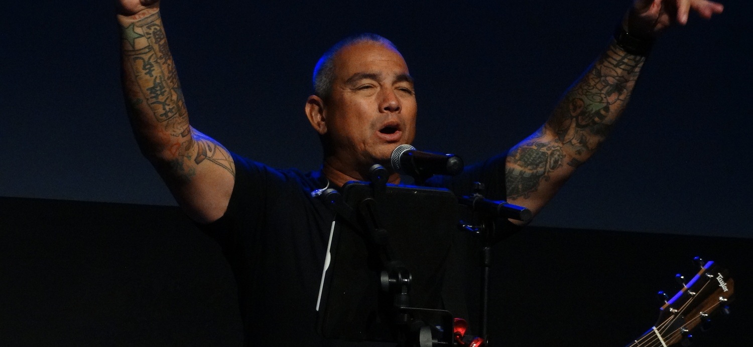 Tattooed musician raising arms while singing