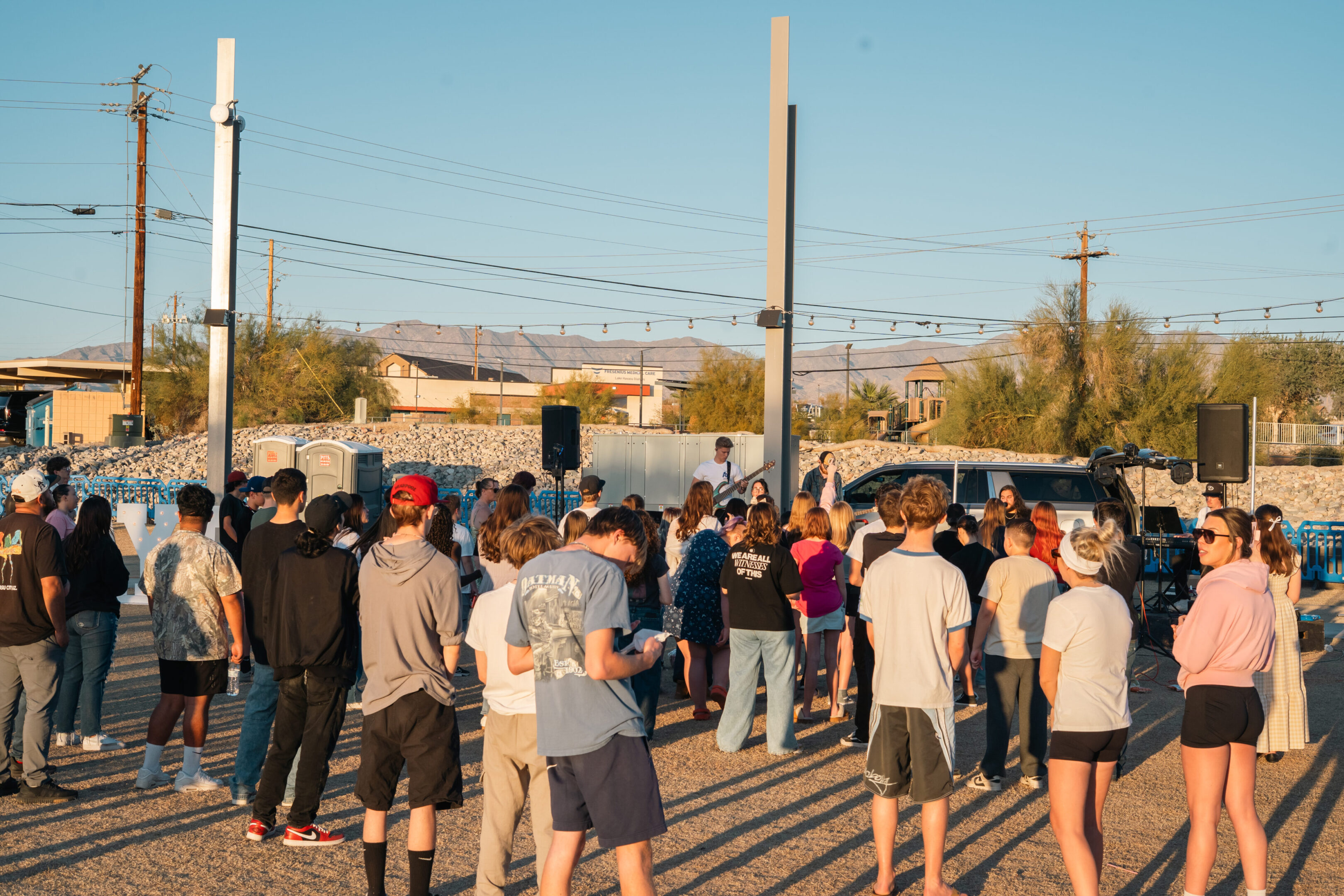 A crowd gathers outdoors during sunset near a barbed wire fence.