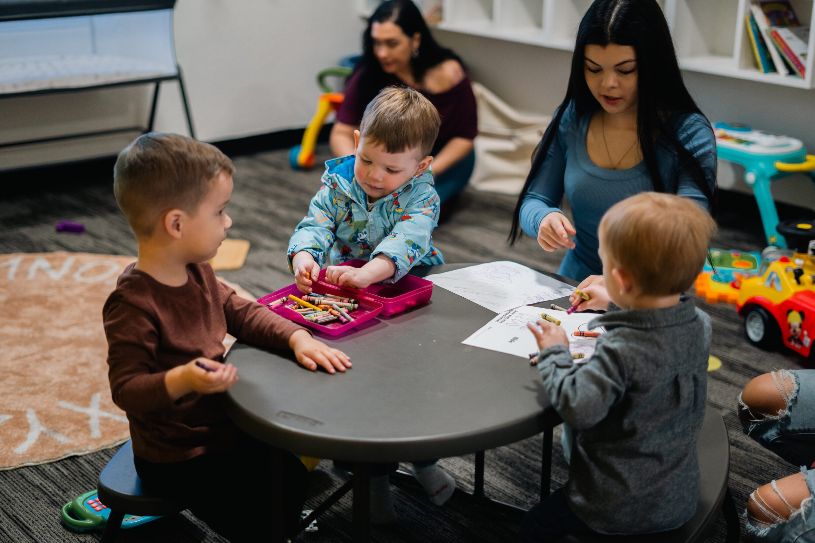 Toddlers engaging in activities at a daycare table with caregivers.