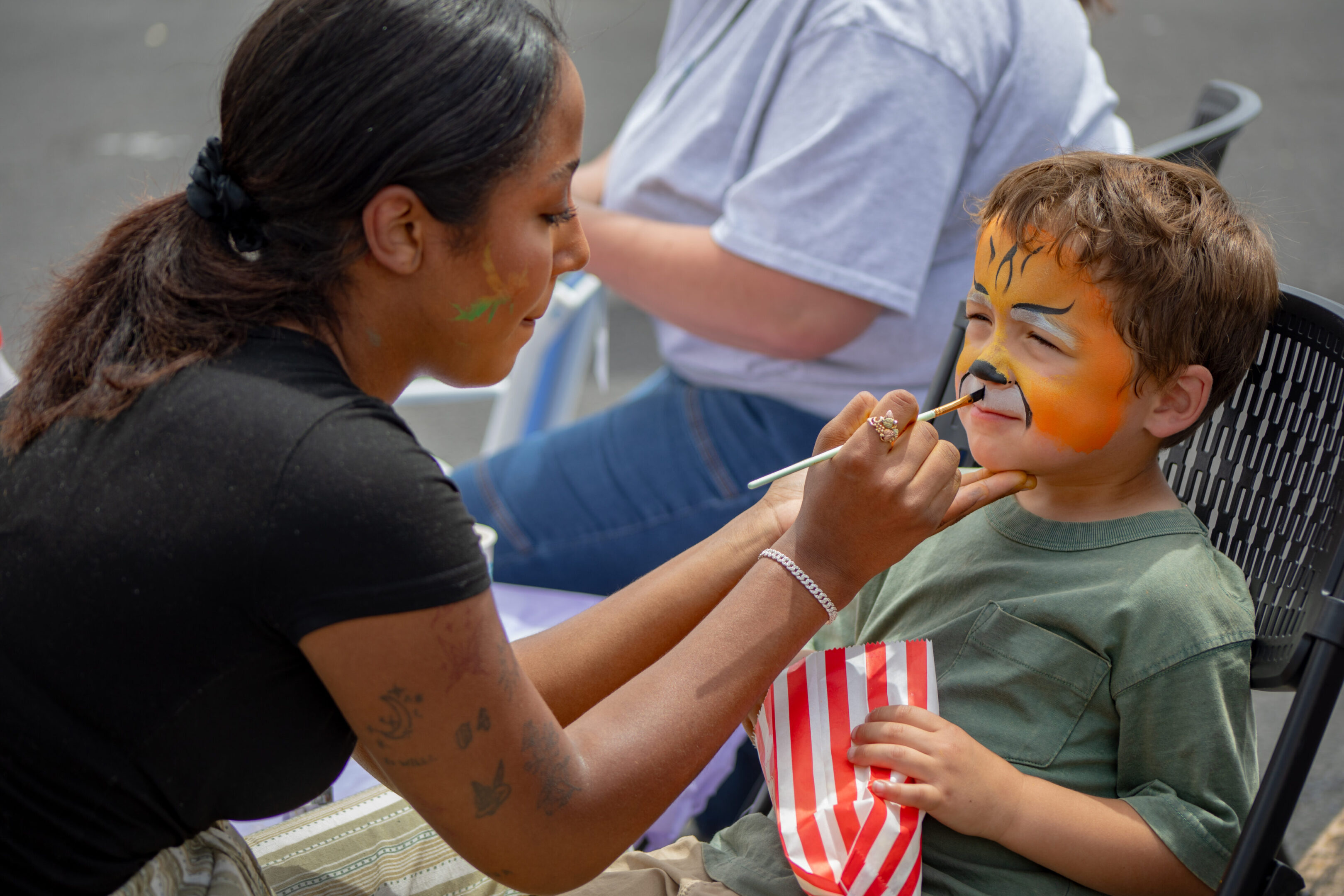 Child getting a tiger face paint at an outdoor event.