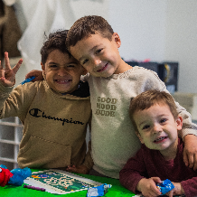Three young boys smiling and posing together indoors.