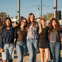 Five friends smiling together outdoors on a sunny day.