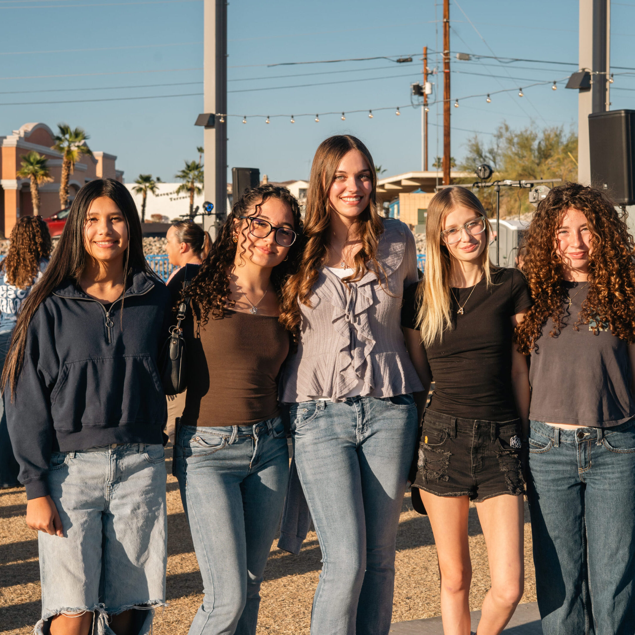 Five young women posing outdoors on a sunny day.